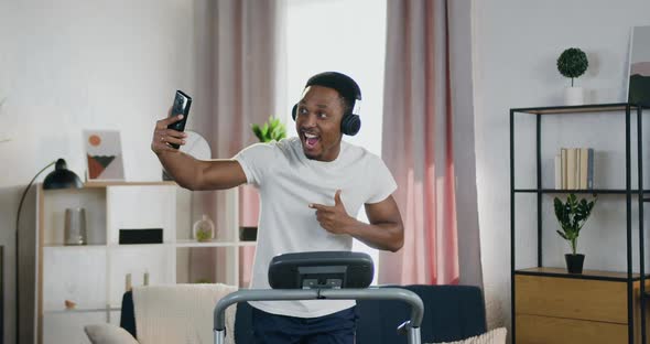 Black-Skinned Guy in Headphones which Running on Treadmill at Home and Making Selfie