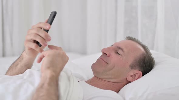 Relaxed Middle Aged Man Using Smartphone in Bed