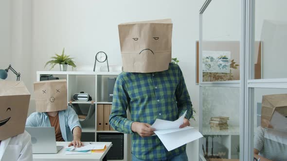 Office Workers with Paper Bag Heads Showing Emoji Working at Project at Desks While Grumpy Boss