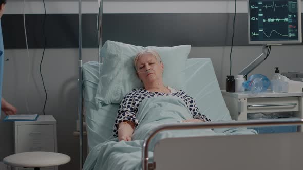 Elder Woman with IV Drip Bag Sleeping in Hospital Ward Bed