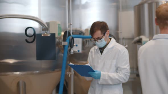 Man in Safety Mask Gloves and Lab Coat with Clipboard Working at Craft Brewery