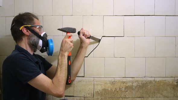 Bearded Middleaged Worker with Tools is Trying to Tear Off an Old White Dirty Tile in a Toilet