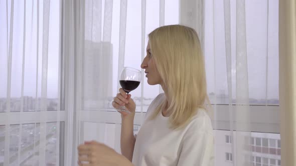 A beautiful girl holds a glass of wine and looks out the window. Wine tasting.