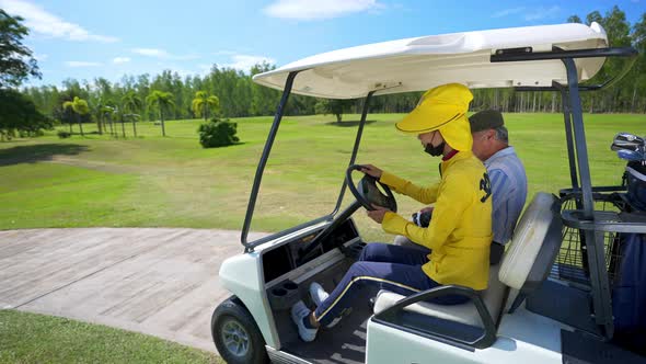 4K Asian senior man driving golf cart on golf course to golfing on the green with female caddy