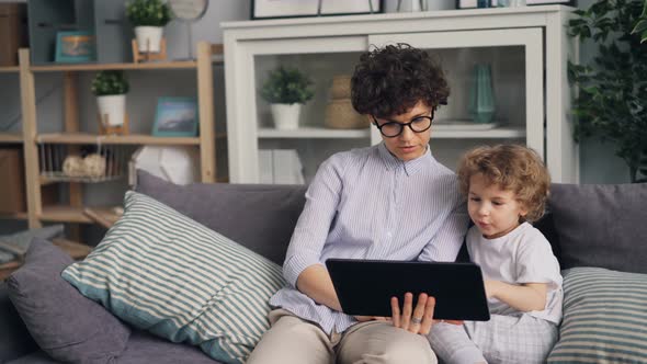 Adorable Boy Watching Cartoons on Tablet with His Caring Mother Holding Gadget