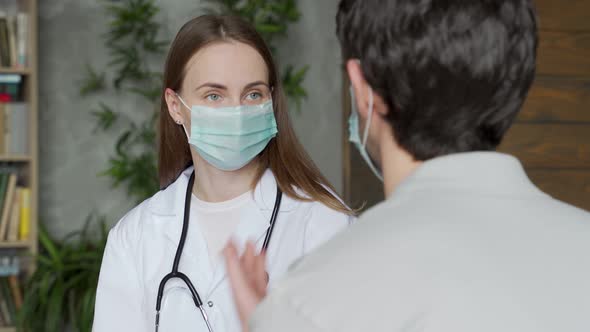 Doctor a Woman in a Medical Mask Talks to a Male Patient Sitting on a Sofa