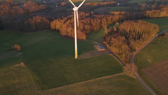 A high windmill spinning fast in a lush, green field at sunset. Cinematic aerial orbit shot