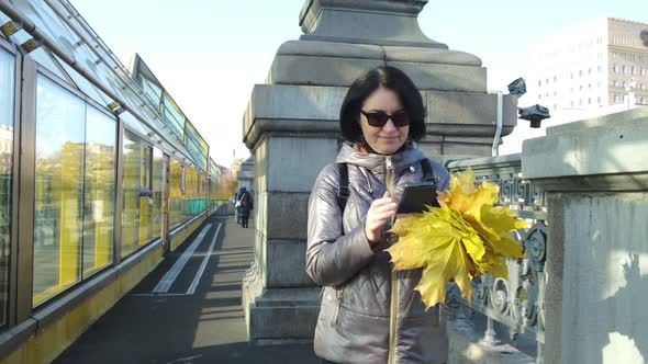 A Middleaged Woman a Brunette Caucasian Race with a Bouquet of Yellow Leaves Walks Across the Bridge