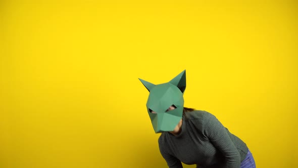 A Young Woman in a Cardboard Jackal Mask Looks at the Camera on a Yellow Background. Woman in Green