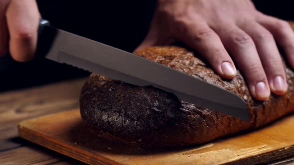 Cutting Crispy Artisan Bread with a Knife in the Kitchen on a Sunny Day Against the Background of