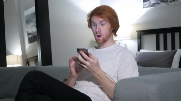 Redhead Man Excited for Success While Using Smartphone