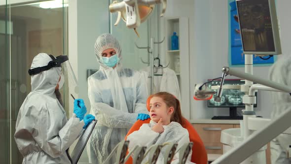 Dentist Doctor in Ppe Suit Taking Notes on Clipboard About Little Patient