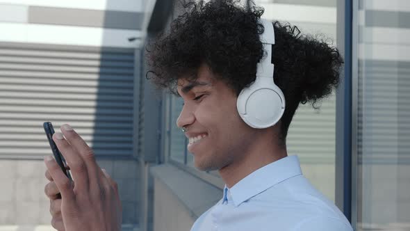 Happy Afro American Messaging Online with Mobile Smartphone While Listening Music with Headphones