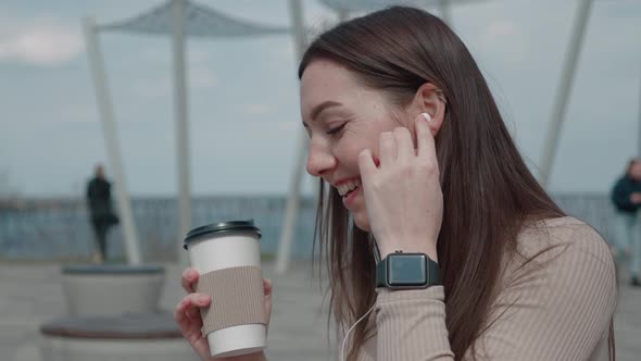 Carefree Beautiful Woman in the City Park Holding Coffee and Listening to Music on Headphones