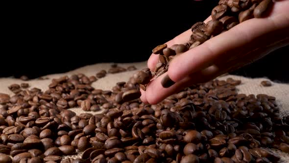 Hand mixing roasted coffee beans. Slow motion of arabica coffee seeds.