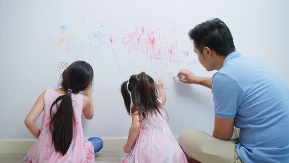 Asian young sibling kid girl enjoy paint on white wall with father.