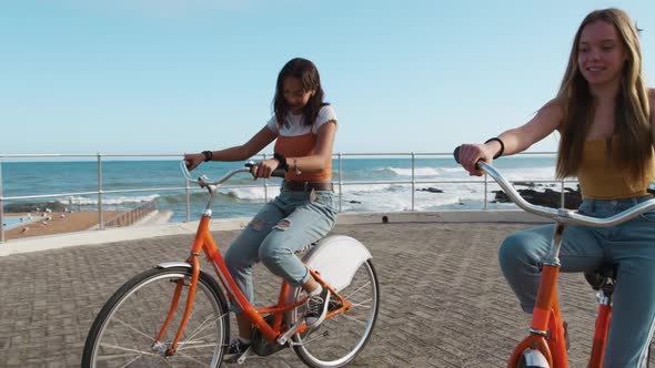 Side view of a Caucasian and a mixed race girl riding a bike seaside