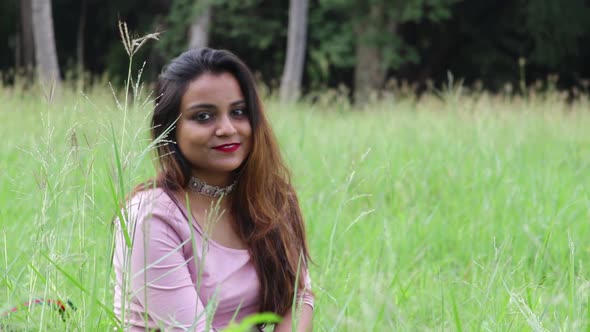 Beautiful Indian woman sitting in tall grass field smiling then look up to the camera.