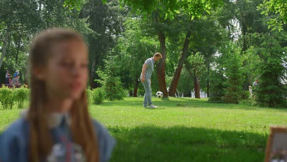 Young Father Passing Ball Active Son Behind Resting Daughter in Park