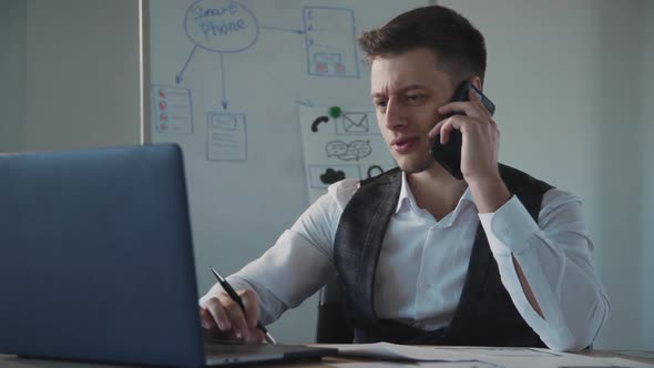 American Young Businessman Talking Phone Working with Laptop at Table in Company