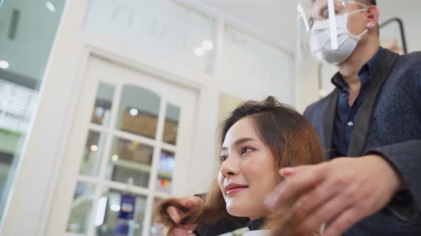 Professional male stylist wearing mask and face shield and cutting customer woman's hair in salon.