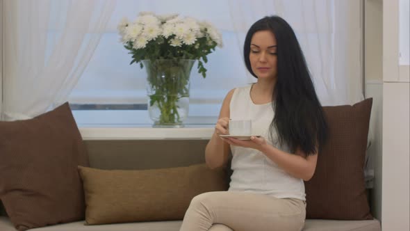 Young Brunette Sitting on Sofa Drinking Tea From Cup in a Office