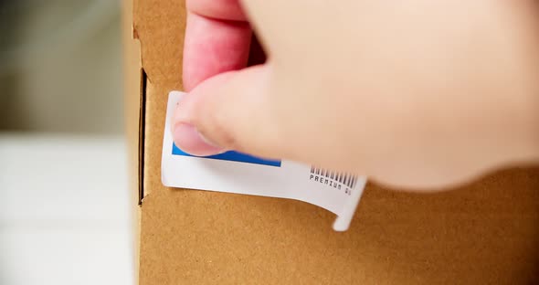 Hands applying MADE IN EL SALVADOR  flag label on a shipping cardboard box with products. Close up s