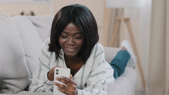 Young African American Woman Lying on Couch Resting Relaxing Chatting on Video Call Using Smartphone