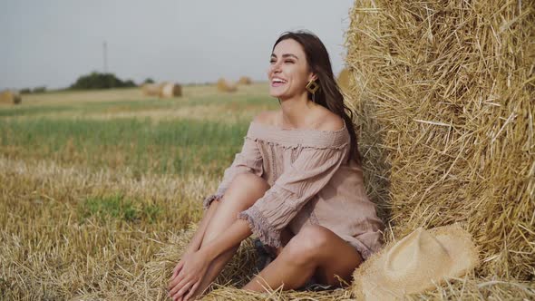 Woman in Summer Dress Resting at a Haystack in a Field and Talking with Laugh