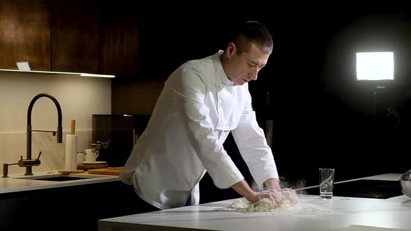 baker works in kitchen of bakery shop. cook mixes flour with egg  with hands.