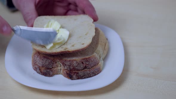 Close up view of man spreading butter on bread with knife.