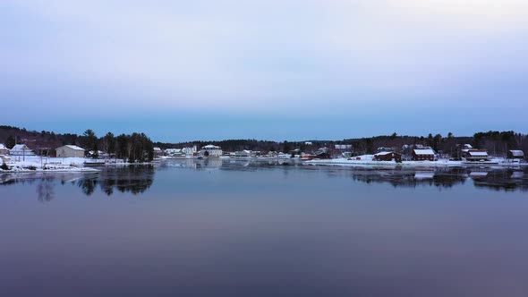 Aerial footage flying low over a skim of ice on Moosehead Lake towards downtown Greenville Maine