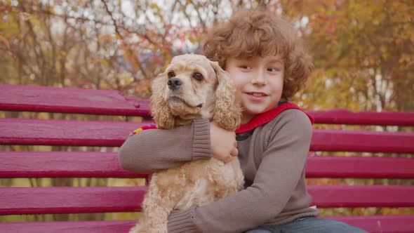 Happy Boy Embracing Cocker Spaniel Dog on Bench in Autumn Park