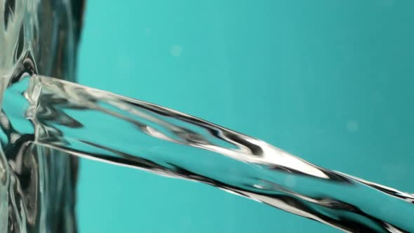 Close Up Footage in Slowmotion of Flowing Stream of Clear Water Over Cyan Background