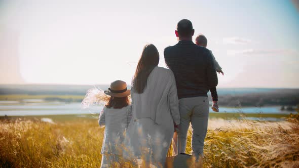 Young Family with Little Baby and Girl Standing on the Field and Looking Into the Distance