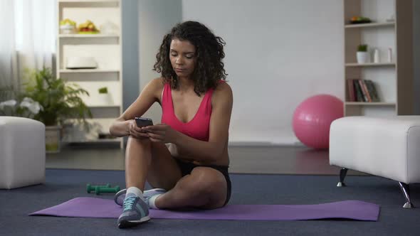 Female Sitting on Floor in Sportswear, Using Cellphone Tracking Application