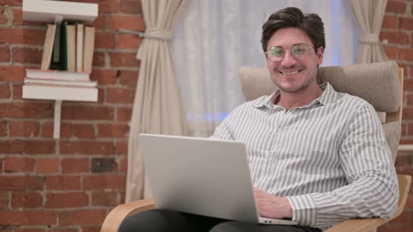 Middle Aged Man with Laptop Smiling at Camera on Sofa