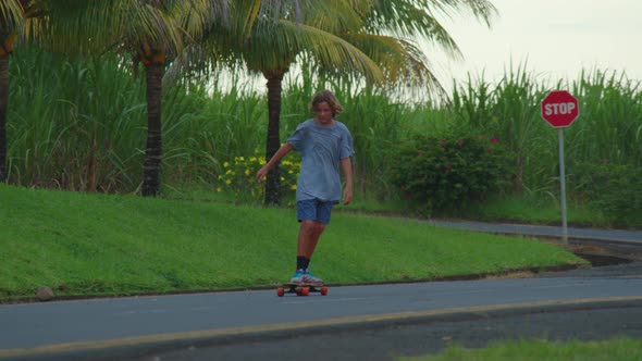 A Teenager Rides a Longboard Along a Beautiful Road with Green Palm Trees