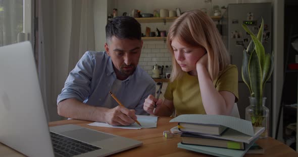 Young Dad Helping Teenage Daughter Schoolgirl Study Online at Home Sitting at Kitchen Table at Home