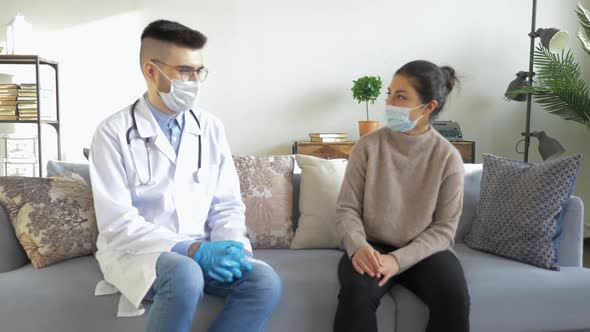 Health visitor examining a woman during home visit at home while man is couching during covid-19