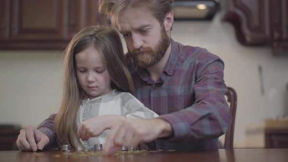 Close Up Portrait of Bearded Man Sitting at the Table in the Kitchen with His Daughter Counting