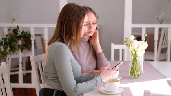 Two young women in cafe looking at mobile phone and chatting