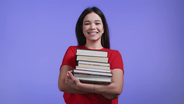 Student Girl Holds Stack of University Books From Library on Violet Background in Studio