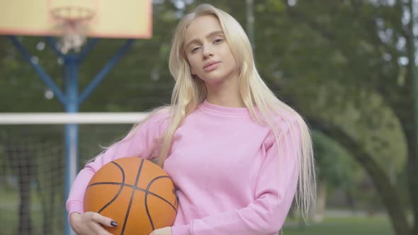 Middle Shot of Young Confident Basketball Player Posing with Ball Outdoors. Portrait of Happy