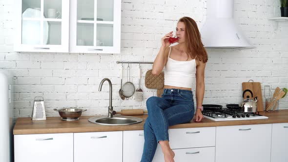 Young woman drinks juice from a glass in the kitchen. Healthy food, diet.