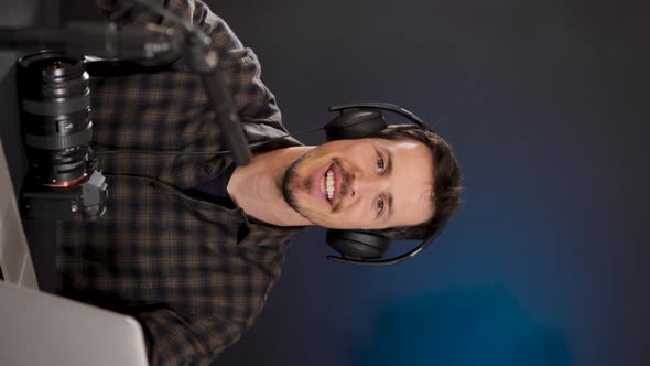 Cheerful guy inn headphones using laptop while recording vlog in studio