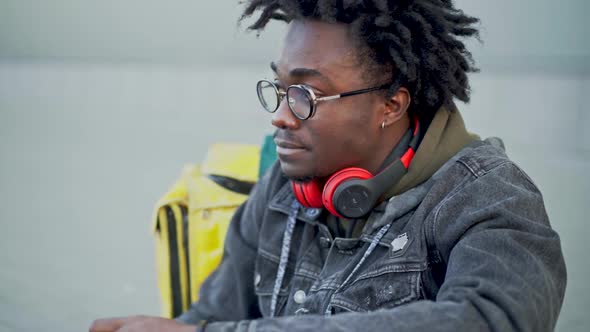 Side View Portrait of Relaxed African American Courier Having Lunch on Urban City Street with