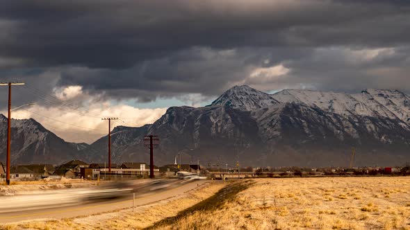 Dramatic clouds roll by the rugged snow capped mountains as rush hour traffic zooms along the highwa