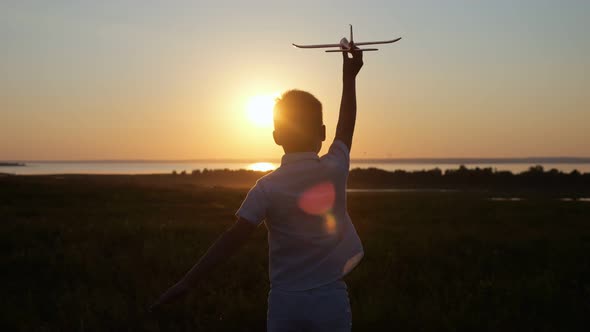 Junior Schoolboy Runs on Meadow to Launch Airplane to Sunset