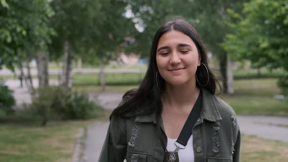 Cheerful Hipster Girl Goes and Dances in the Park To the Music While Holding a Portable Speaker in